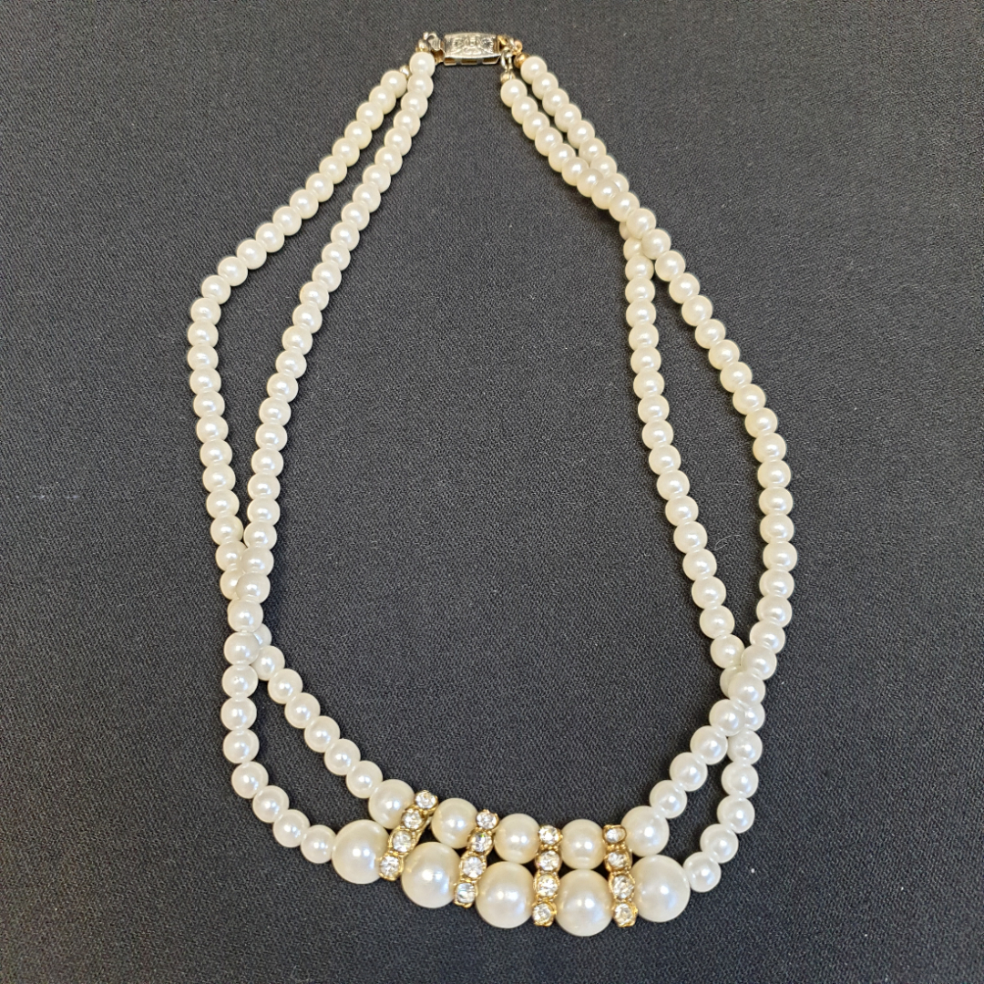Ожерелье из белых бусин с цепочками украшений на белом эстетическом фоне